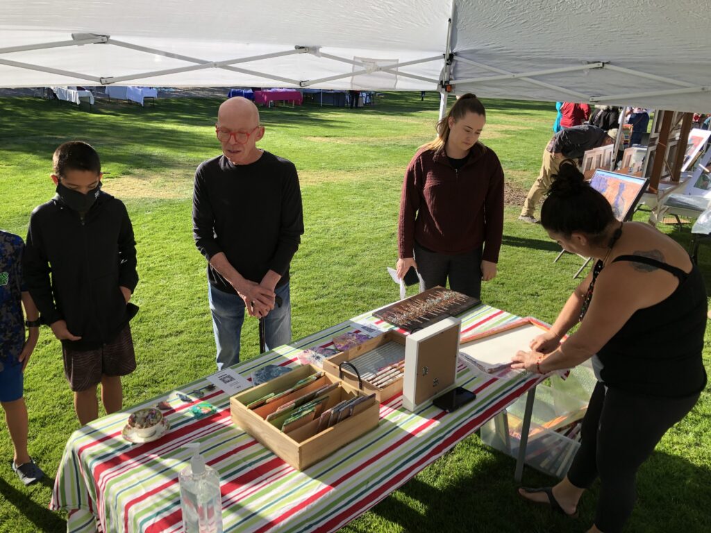 Photo of artist selling art at a booth in a grassy park.